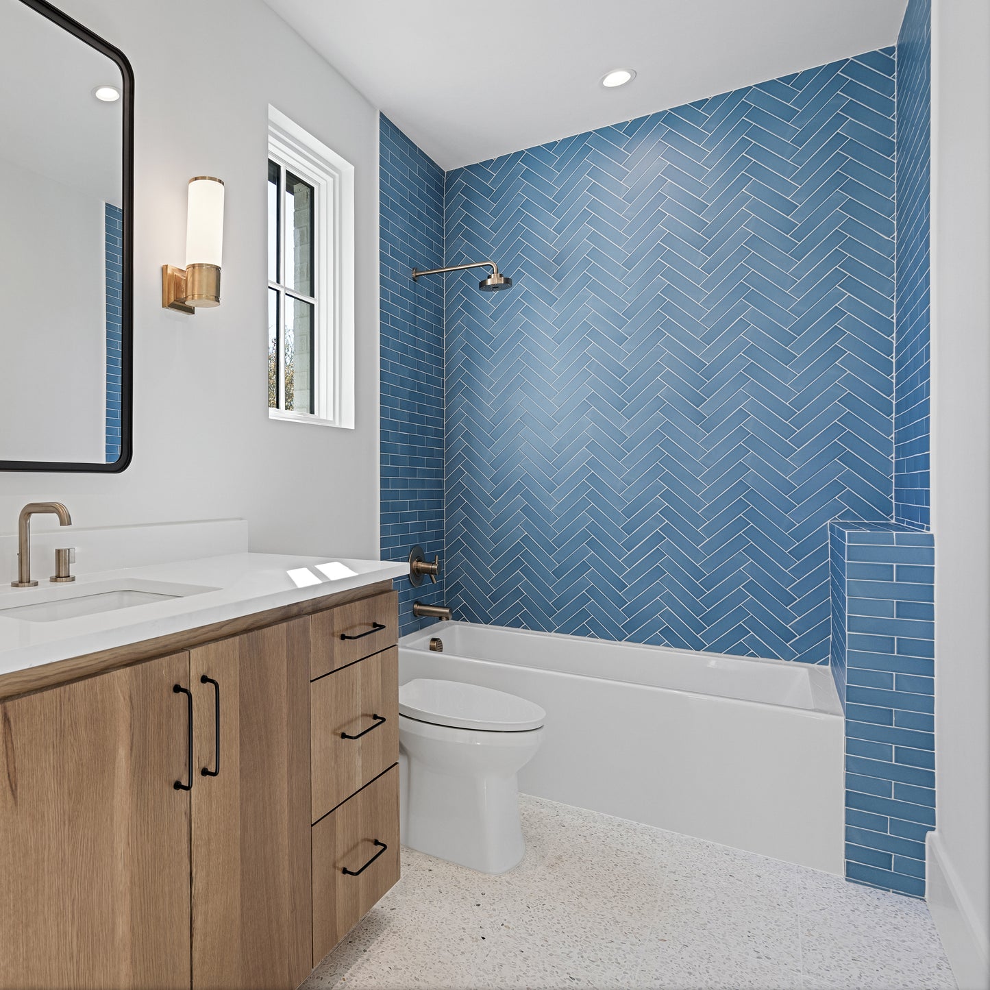 Modern bathroom with blue ceramic herringbone tile, wooden vanity, and white fixtures.