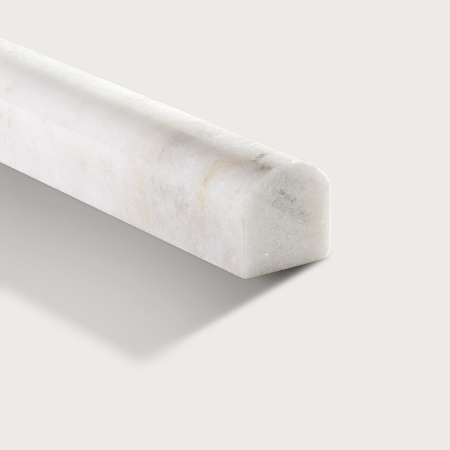 A close-up of a white marble corner trim piece with subtle gray and beige veining, shown on a light beige background.