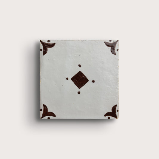 A square zellige tile with a light gray glaze, featuring a central dark brown diamond motif and matching dark brown corner flourishes, shown on a light beige background.