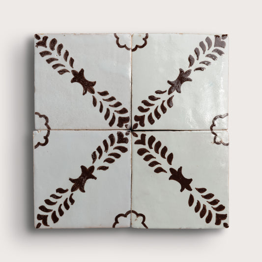 Four square zellige tiles arranged in a 2x2 grid, featuring a glossy off-white glaze with a dark brown hand-painted botanical pattern of leafy stems and star-like motifs.