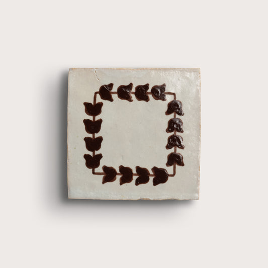 square zellige tile on a light neutral background. feature a dark brown leafy border pattern, and two are plain off-white with brown corner accents.