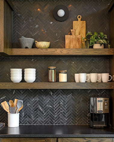 A styled kitchen cabinetry interior with dark wood shelves, a black herringbone tile backsplash, white ceramic mugs and bowls, glass jars, a cutting board, and a small potted plant.