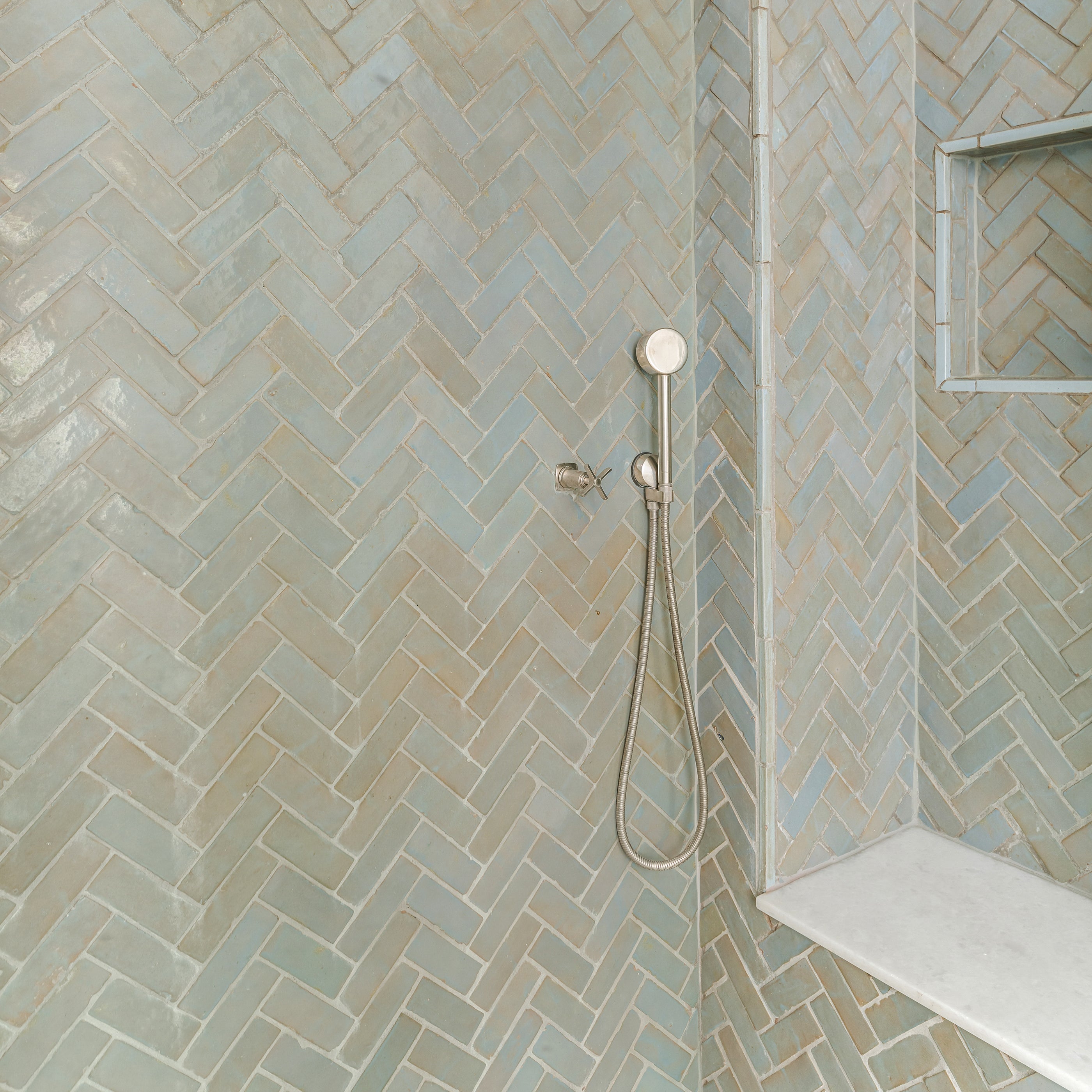 Bathroom shower with blue green zellige tiled walls in a herringbone pattern