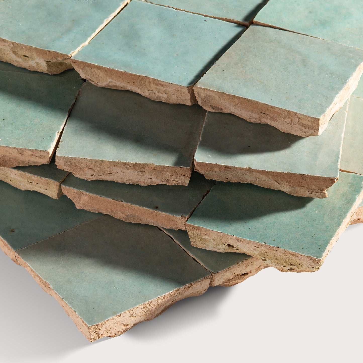 Stack of green zellige tiles with brownish edges on a white background