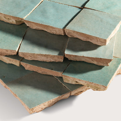 Stack of green zellige tiles with brownish edges on a white background