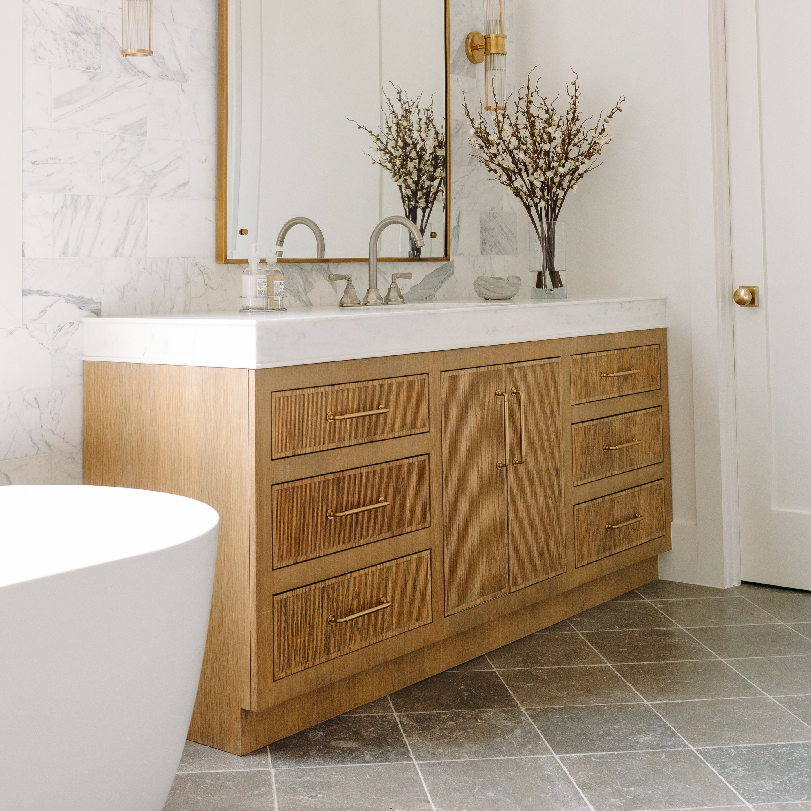 Bathroom with wooden vanity, white countertop, marble wall, and limestone flooring.