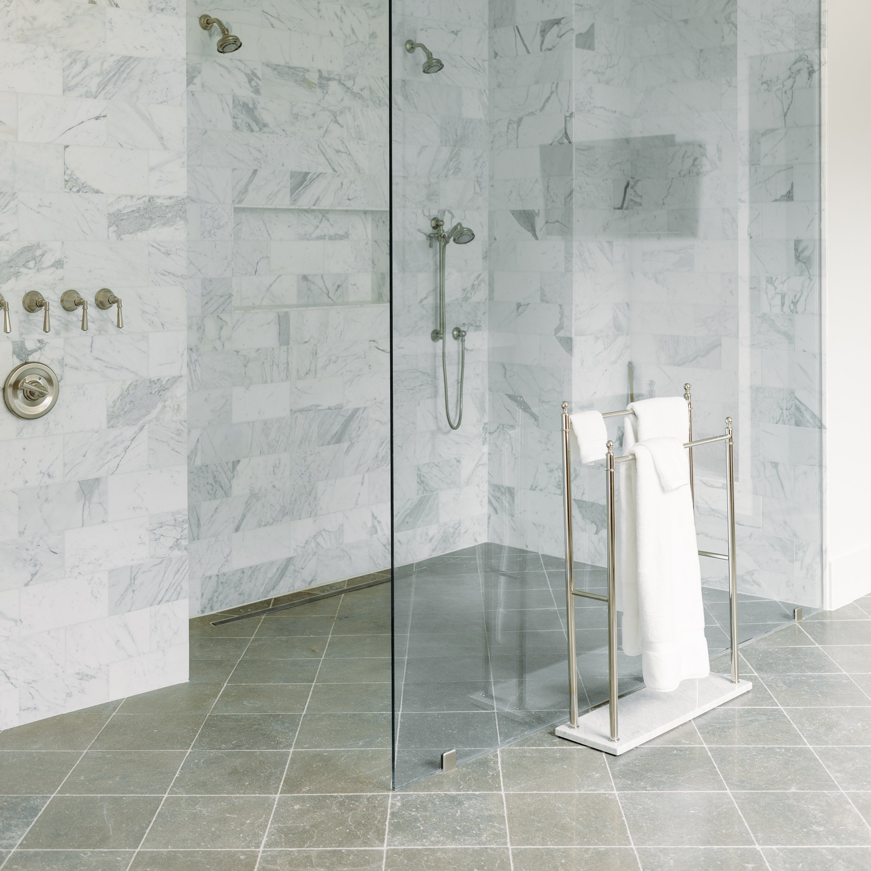 Modern bathroom with marble walls, glass shower enclosure, limestone flooring, and towel rack.