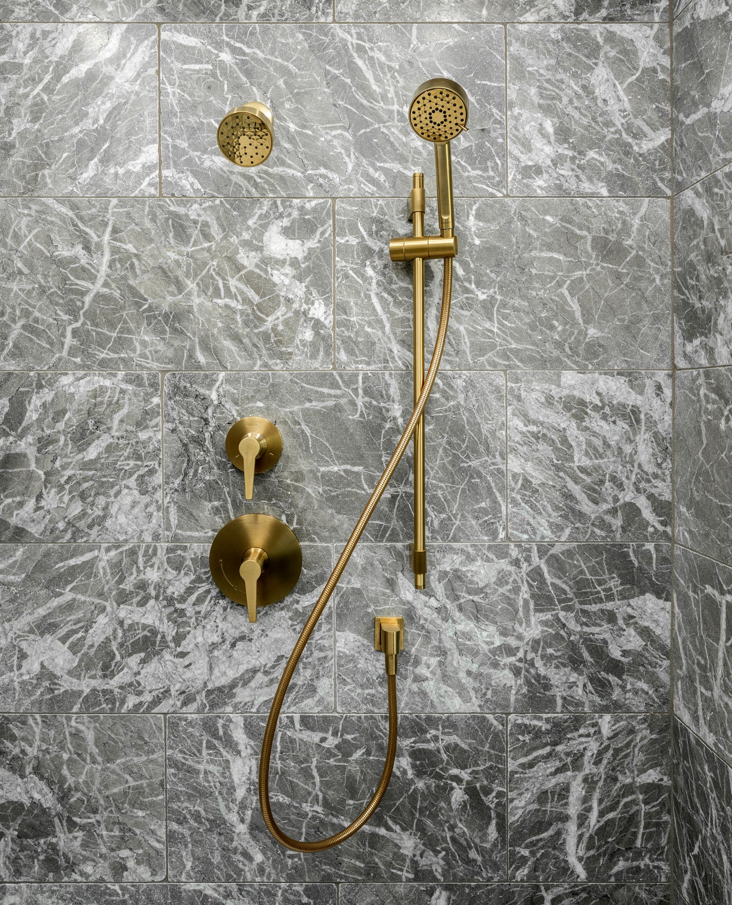 Gold shower system mounted on a gray marble tiled wall