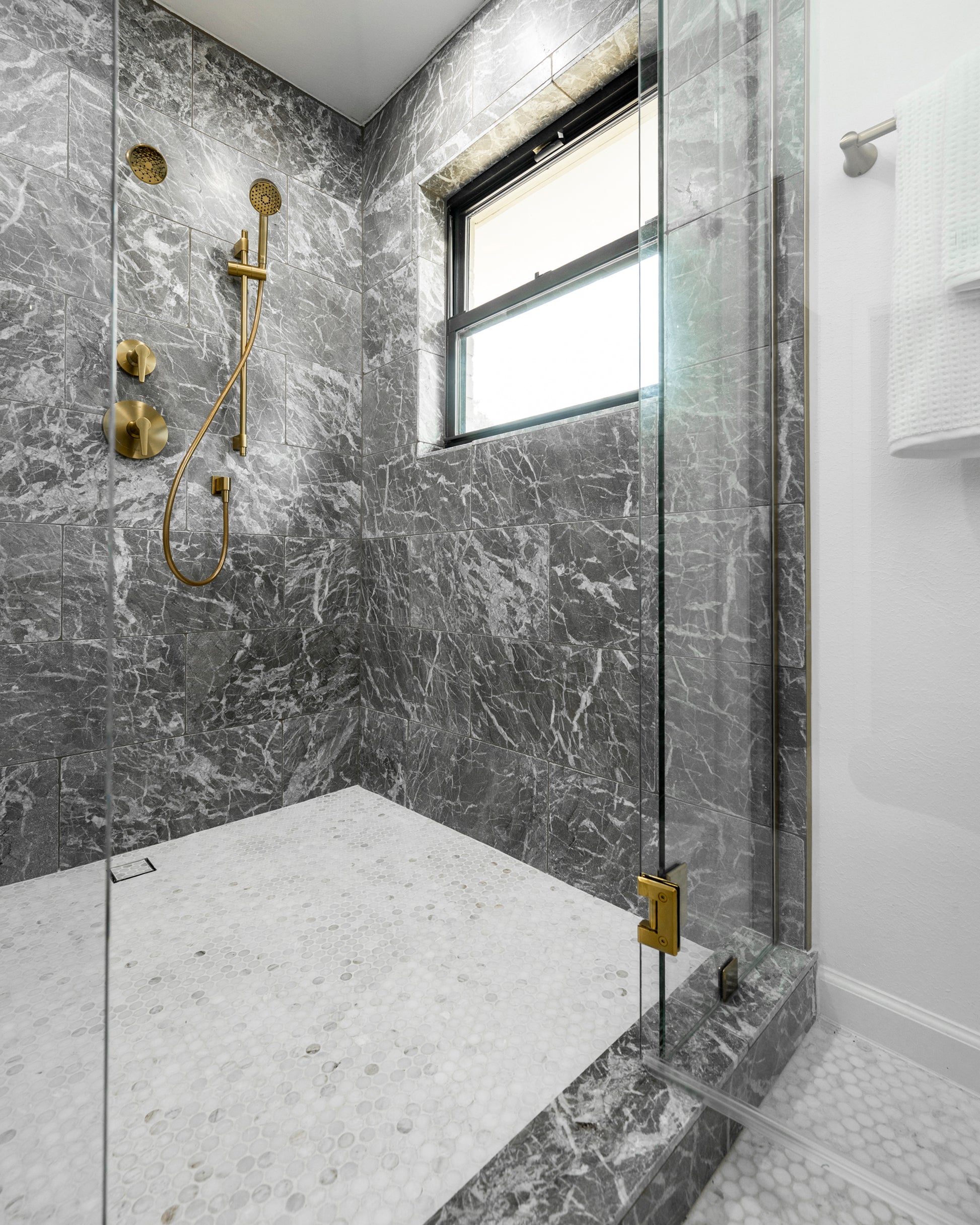 Modern bathroom shower with grey marble walls and gold fixtures