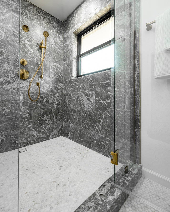 Modern bathroom shower with grey marble walls and gold fixtures