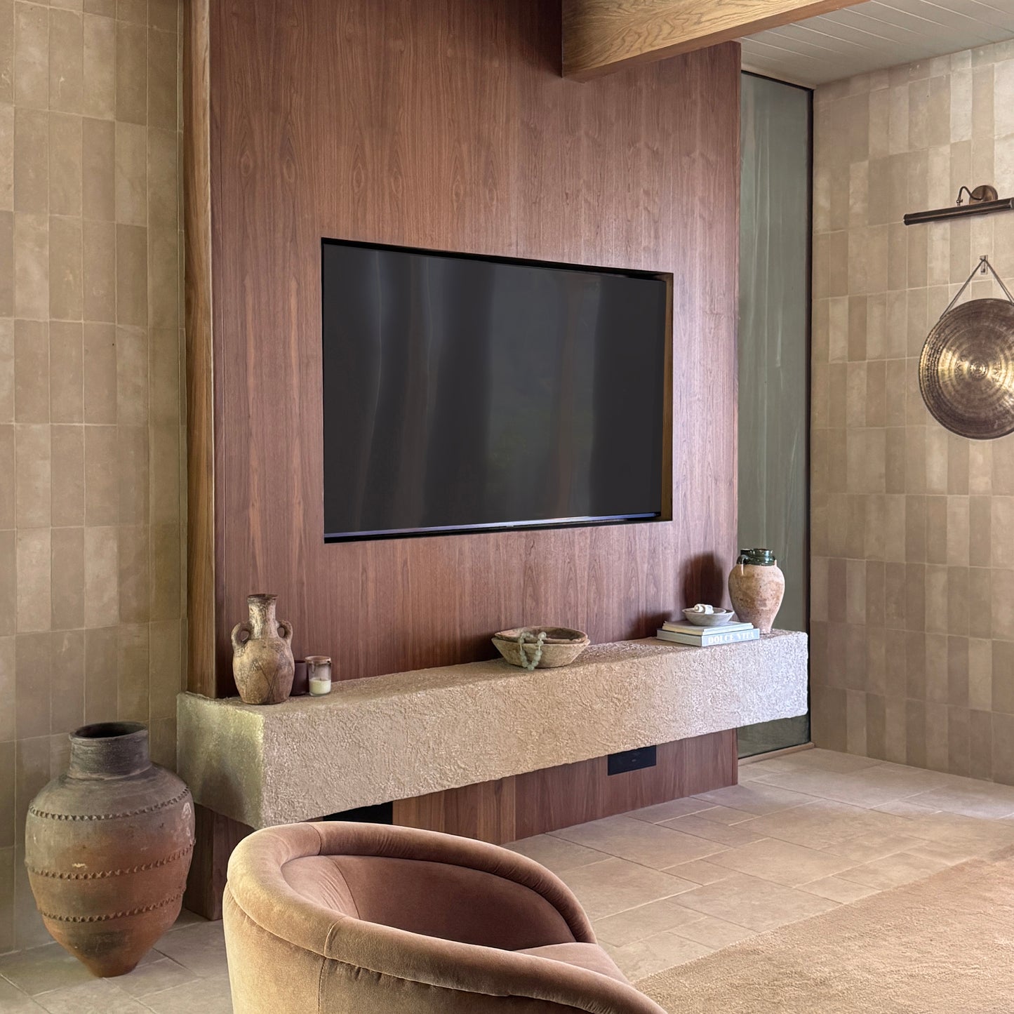 Modern living room with a television mounted on a wooden wall, limestone tiled wall, decorative vases, and a chair.