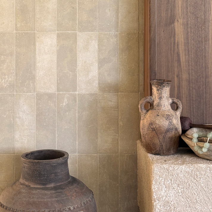 Two vases against a limestone tiled wall with a wooden panel.