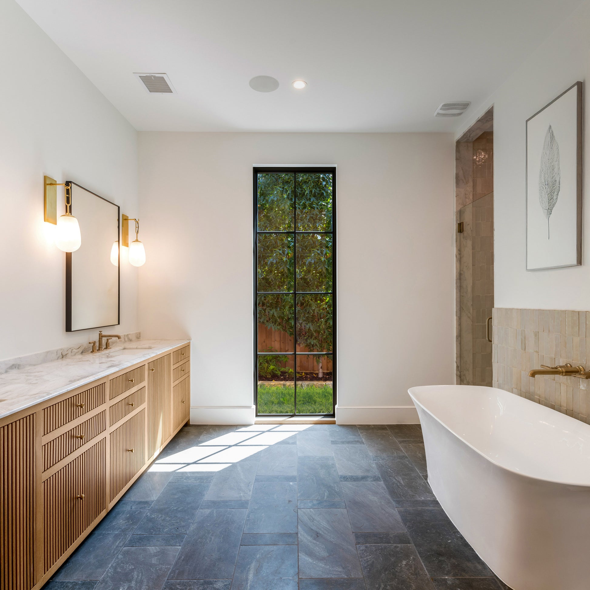 Modern bathroom with freestanding bathtub, wooden vanity, black slate flooring, and large window.