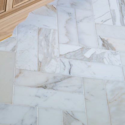 calacatta gold subway tile installed in herringbone pattern on floor of a bathroom