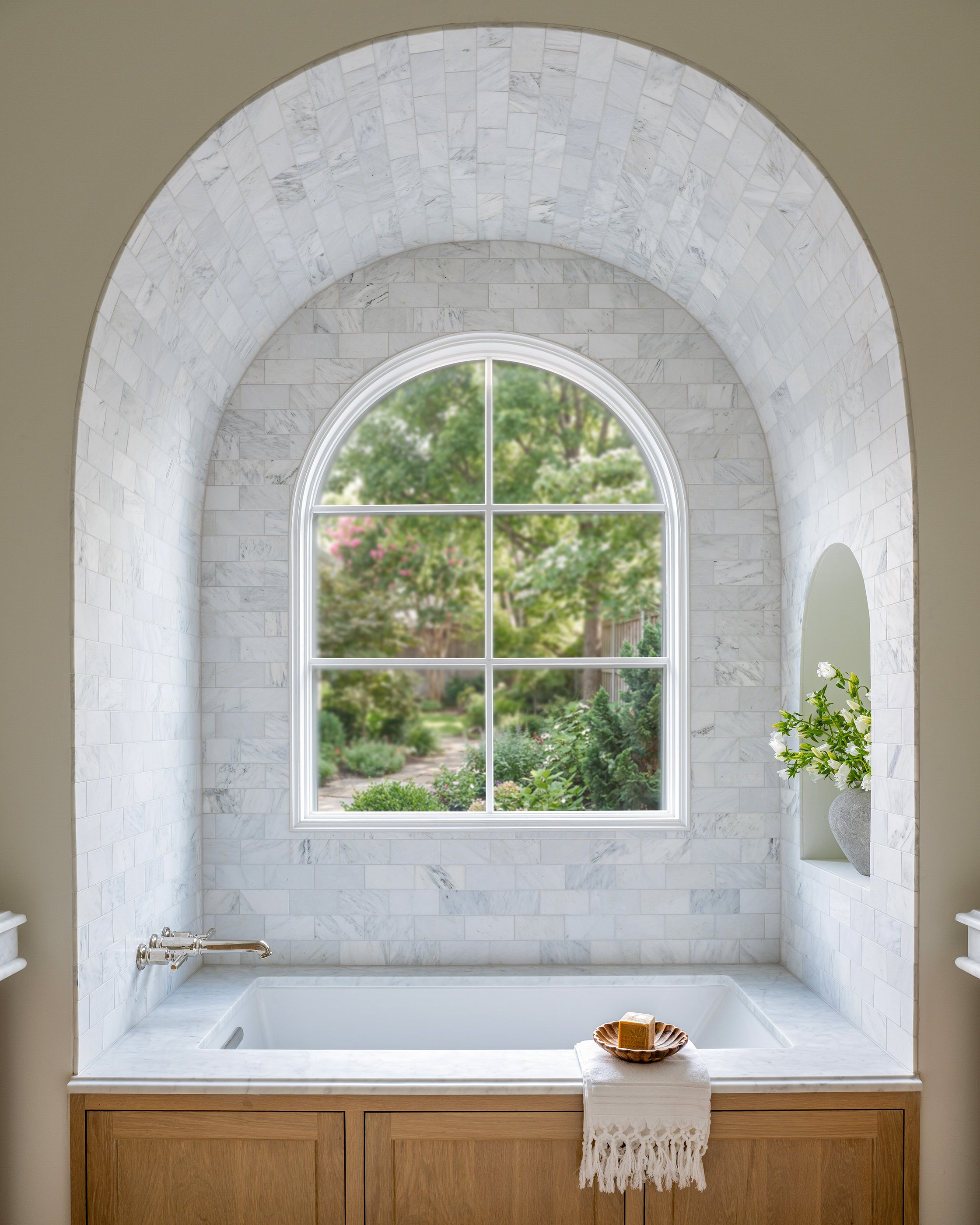Bathroom with marble archway and window, featuring a bathtub and wooden cabinet.
