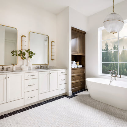 Modern bathroom with white vanity, freestanding bathtub, large window, and marble hexagon floor tile.