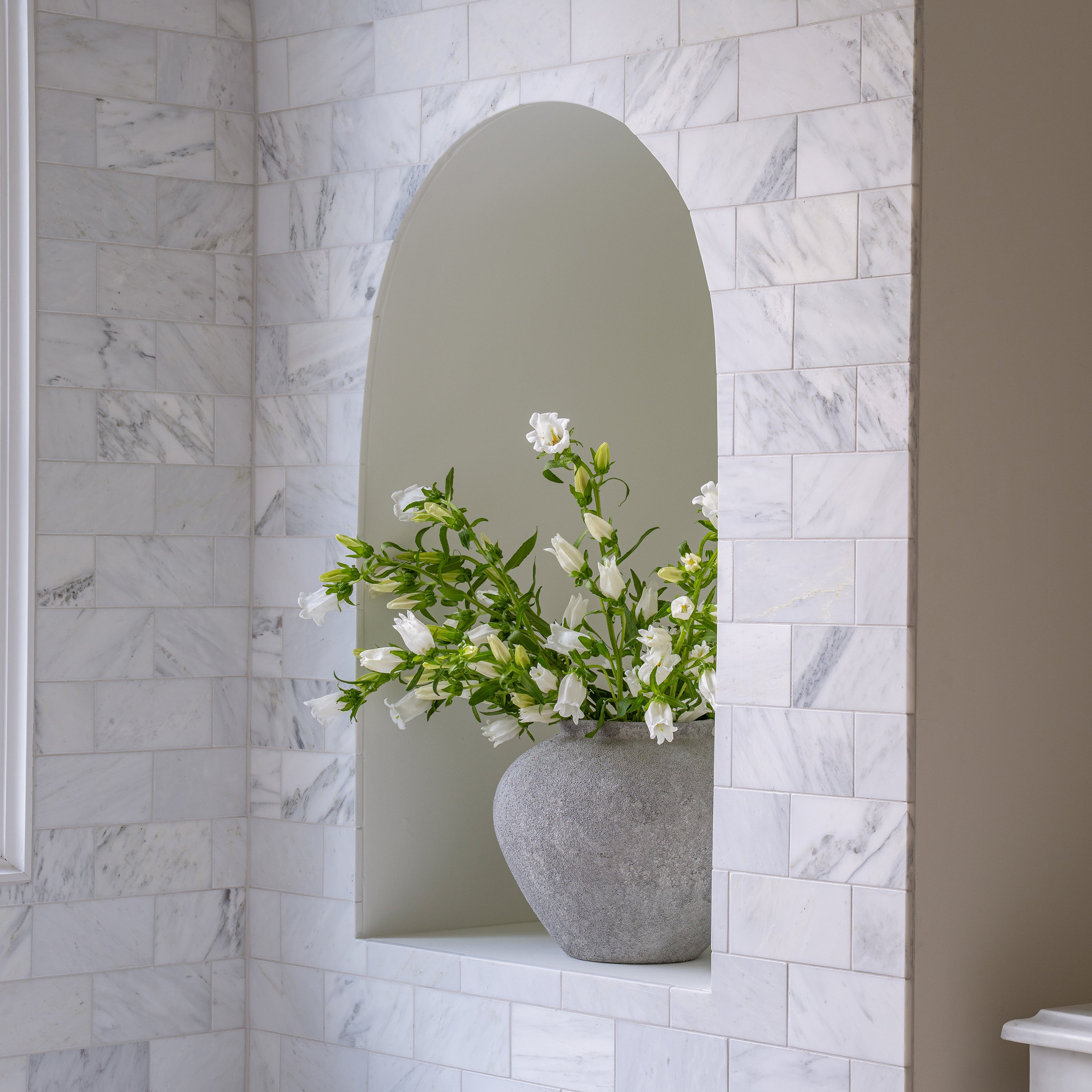 Decorative vase with flowers in a niche against a casablanca carrara marble wall.