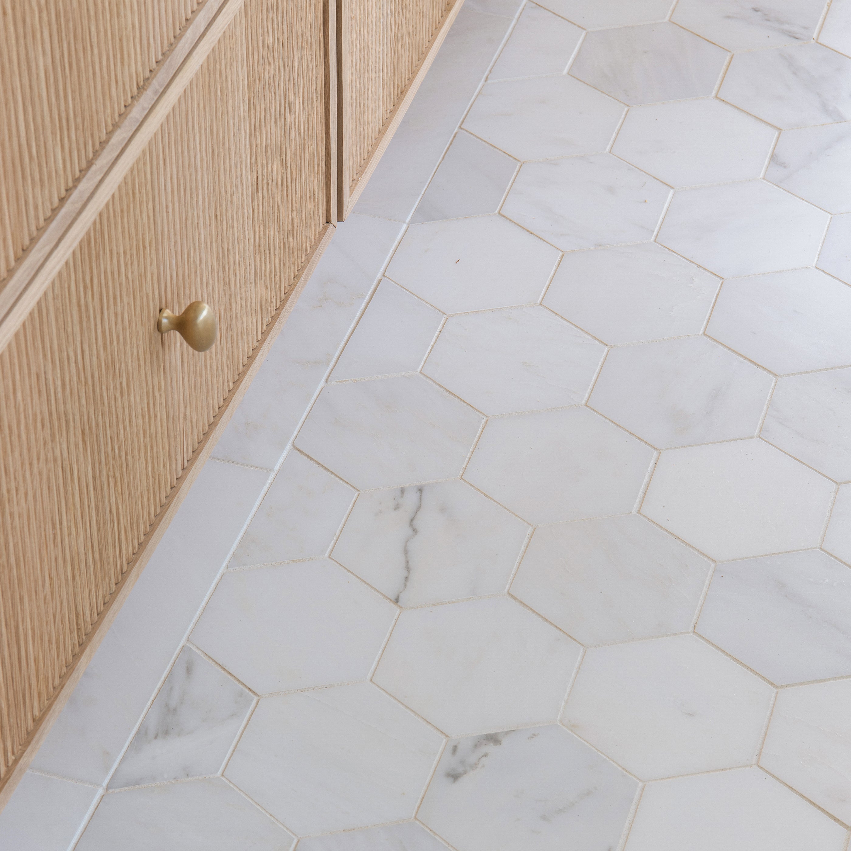 Close-up of a casablanca carrara marble floor with hexagonal tiles and a wooden cabinet