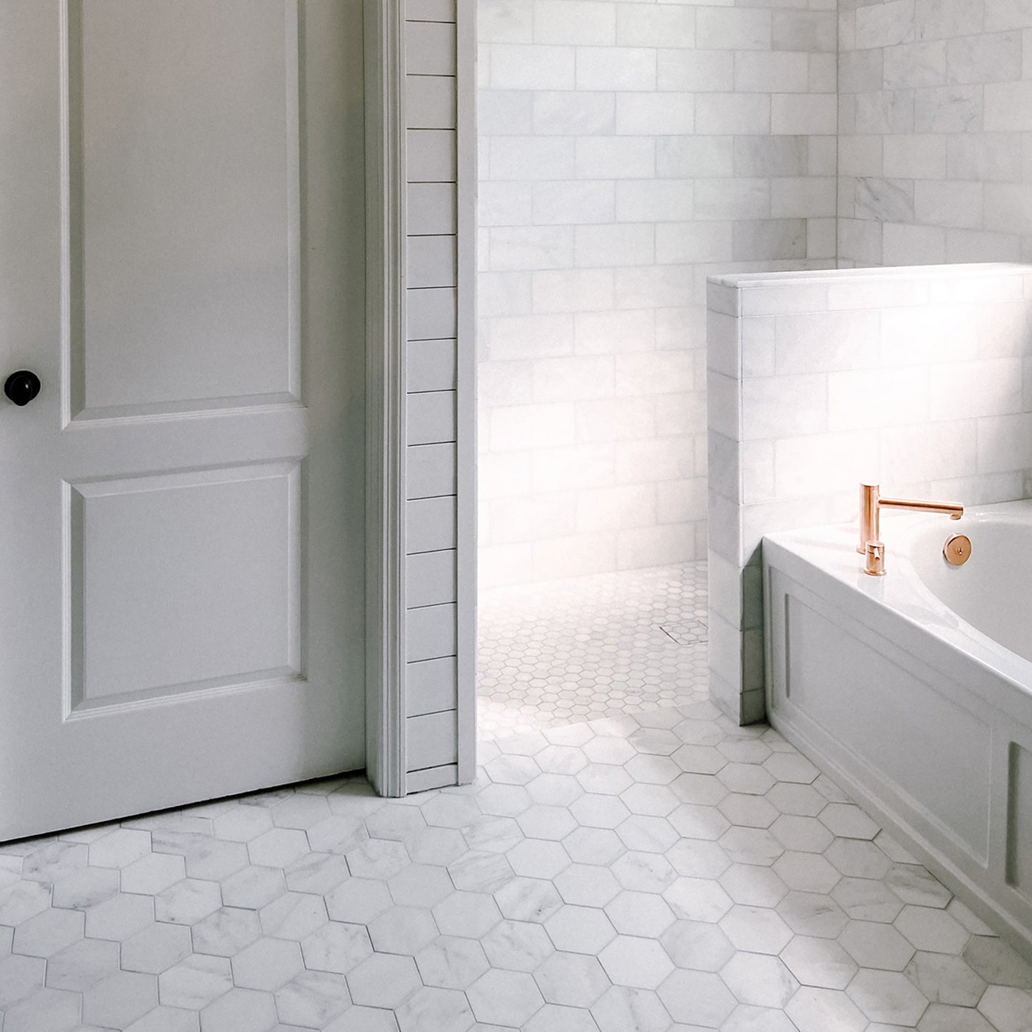 Bathroom with white hexagonal marble tiles on the floor and walls, featuring a bathtub and shower area.