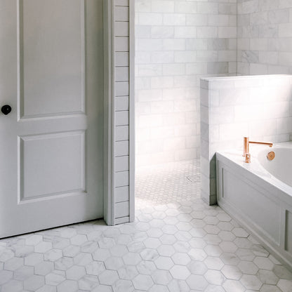 Bathroom with white hexagonal marble tiles on the floor and walls, featuring a bathtub and shower area.