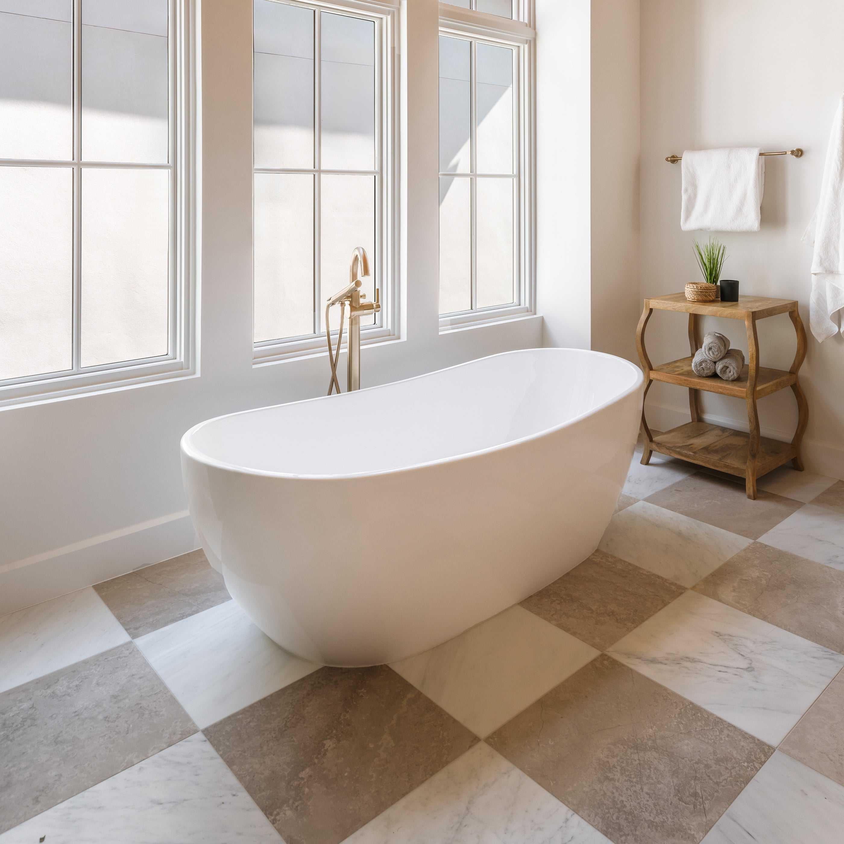 Modern bathroom with a freestanding bathtub in a room with large windows and casablanca gold marble and beige limestone checkerboard flooring.