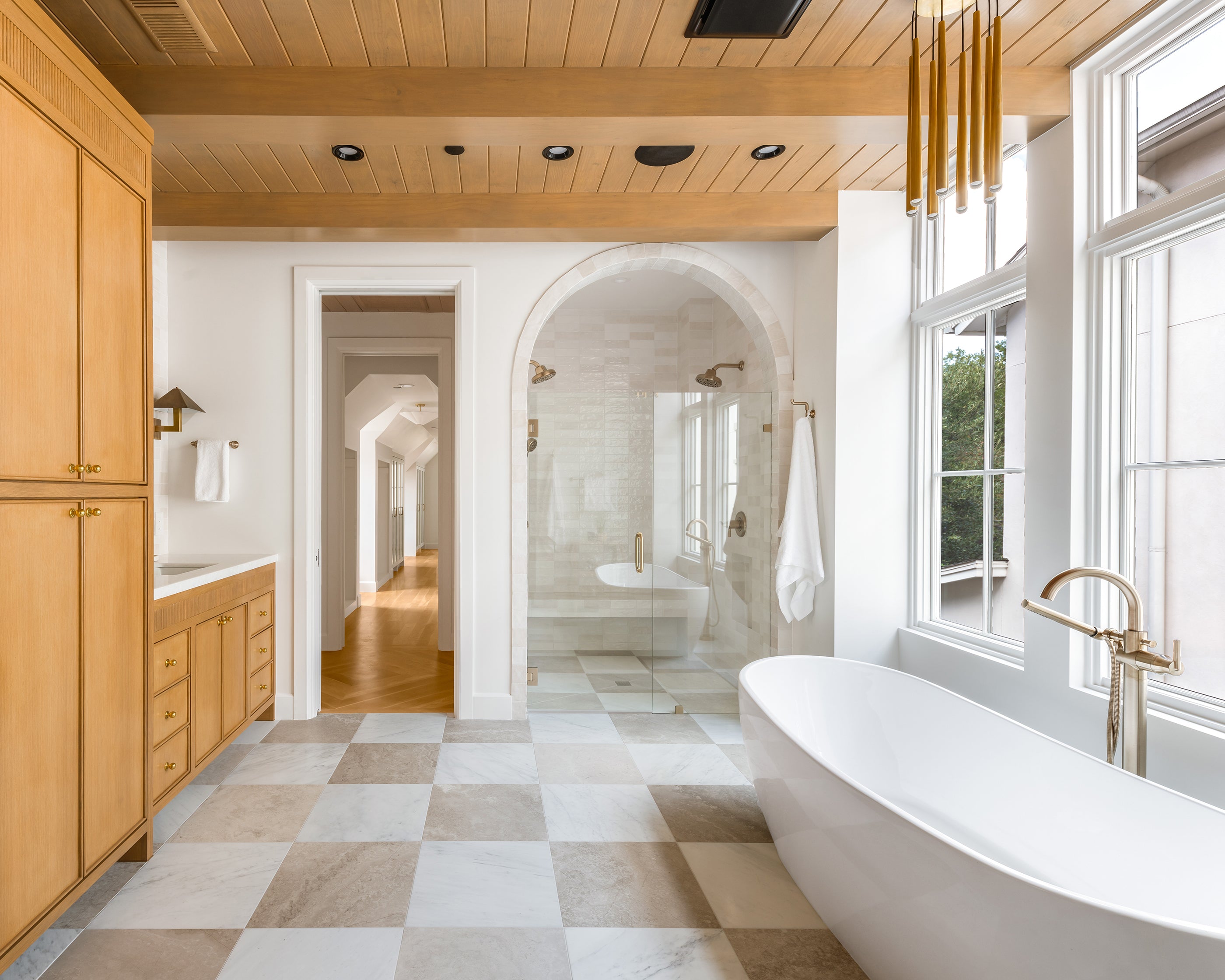 Modern bathroom with a freestanding bathtub in a room with large windows and casablanca gold marble and beige limestone checkerboard flooring.