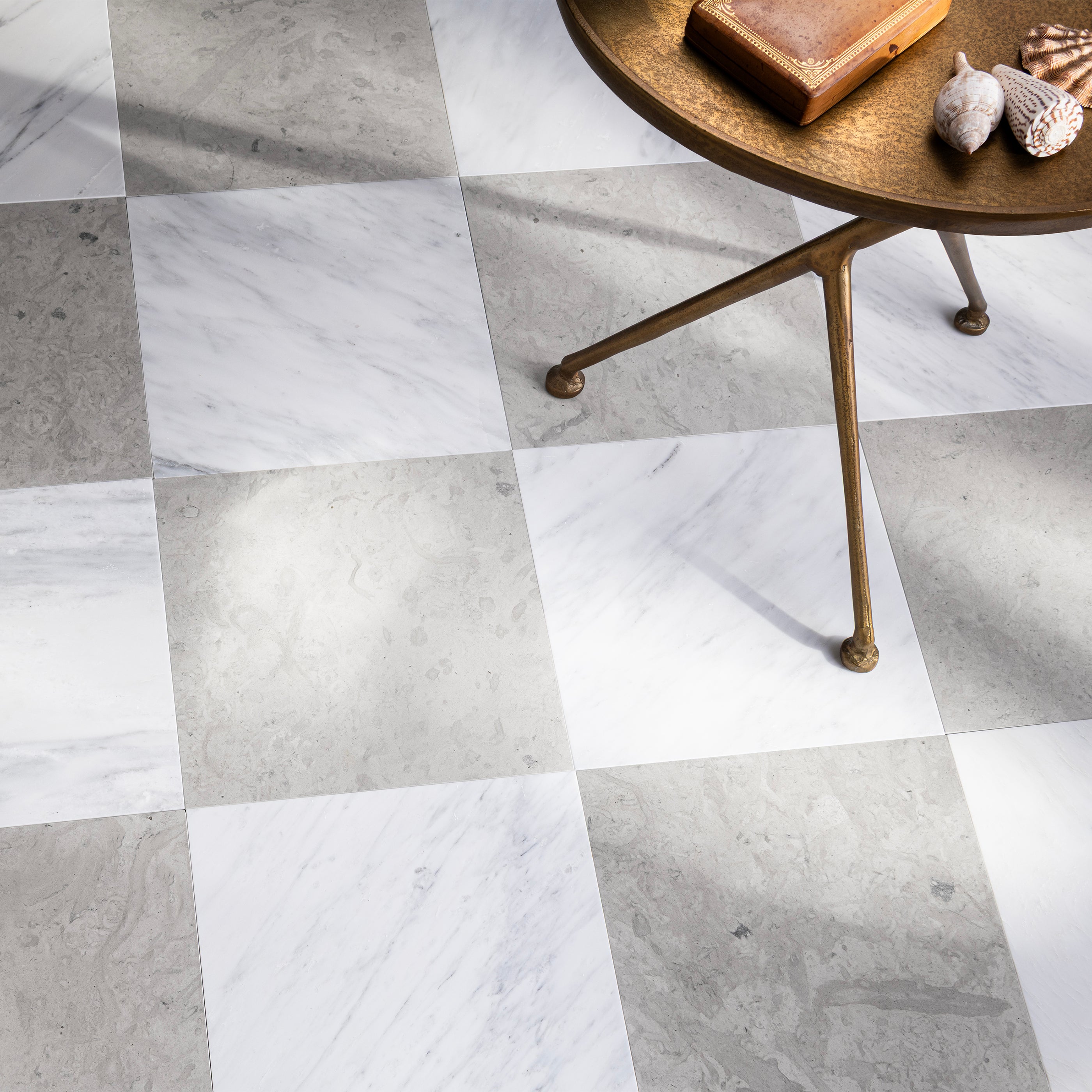 Checkered tile pattern in grey limestone and casablanca gold marble with a small round table and decorative items on a light gray floor.