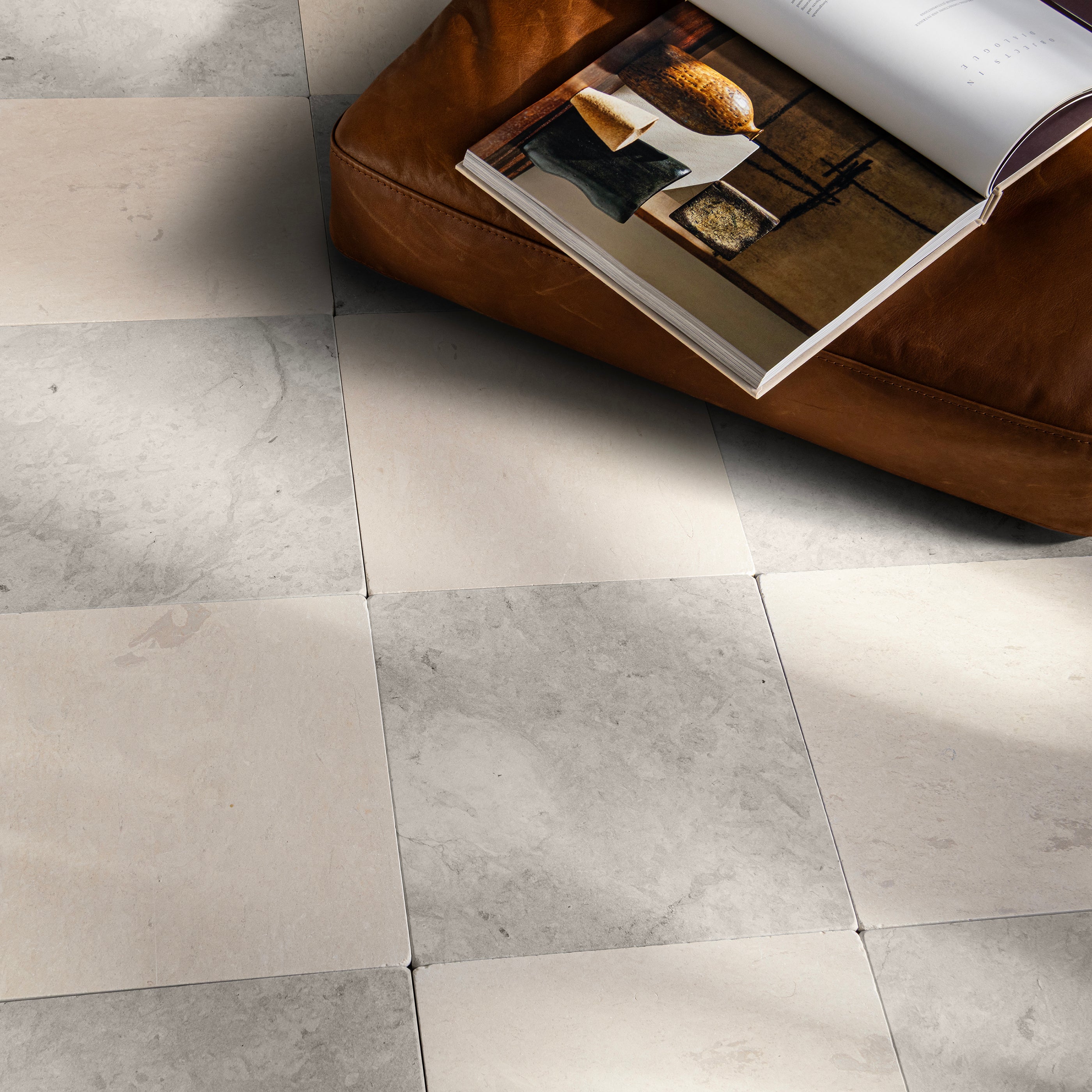 Gray and sand limestone tiled floor with a brown leather ottoman and open book.