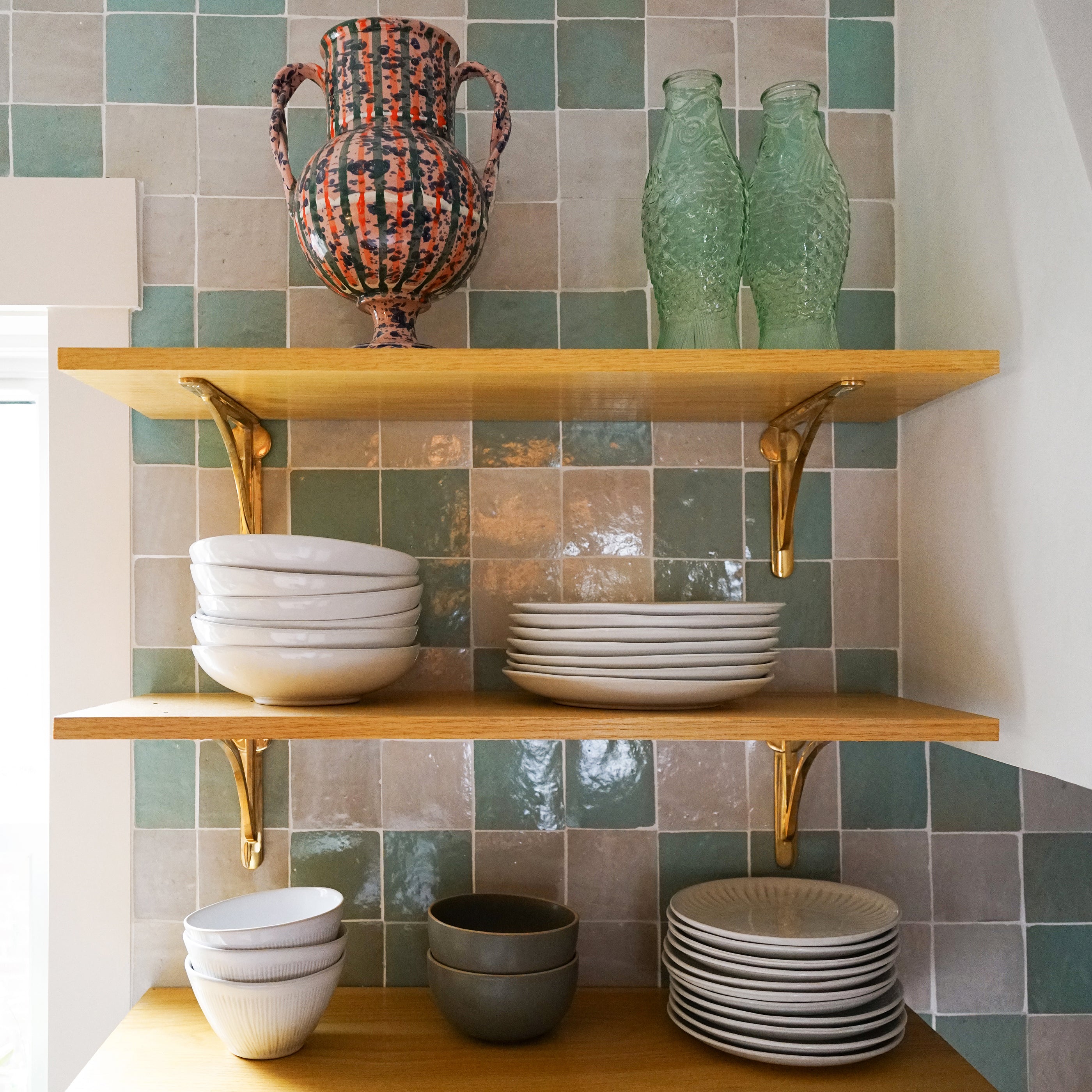 Wooden shelves with ceramic bowls and vases against a zellige tiled wall.