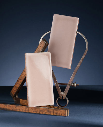 Two rectangular blush pink ceramic tiles displayed on a vintage brass angle ruler against a dark blue studio background.