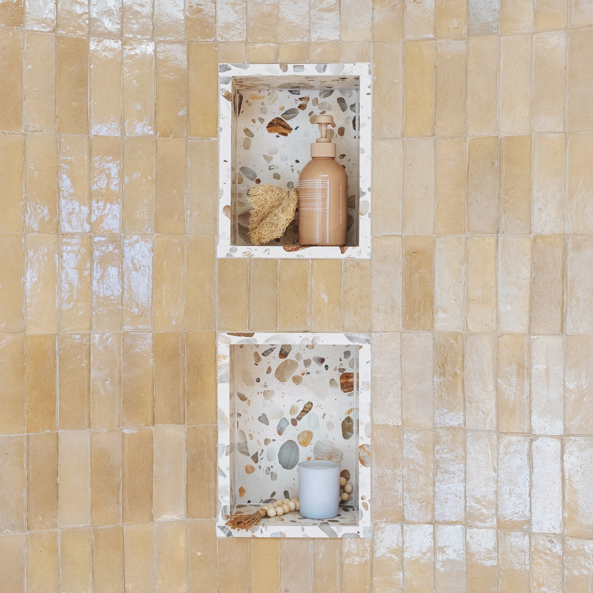 A beige zellige shower tile with two recessed niches containing bath accessories, shown against a matching beige tiled wall.