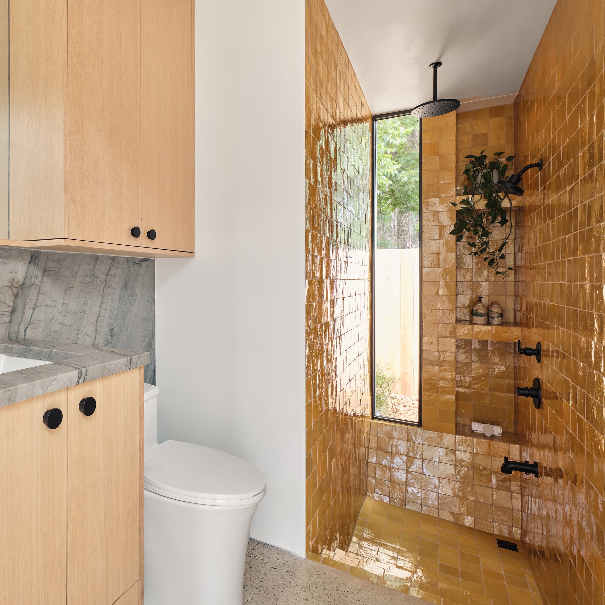 Modern bathroom with wooden cabinets, a toilet, and a shower with gold zellige tiles.