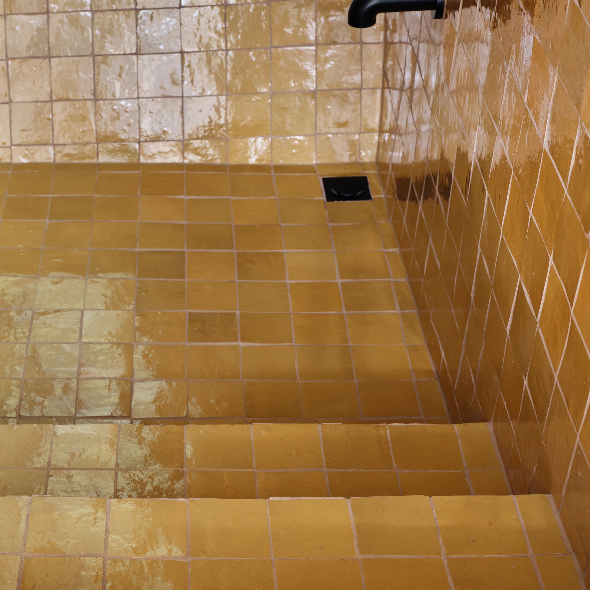 Yellow zellige tiled shower with a drain and faucet