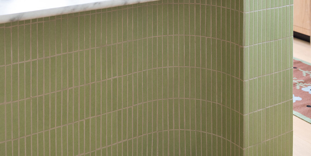 Green ceramic subway tile wall with a marble countertop edge and a patterned rug visible in the background.