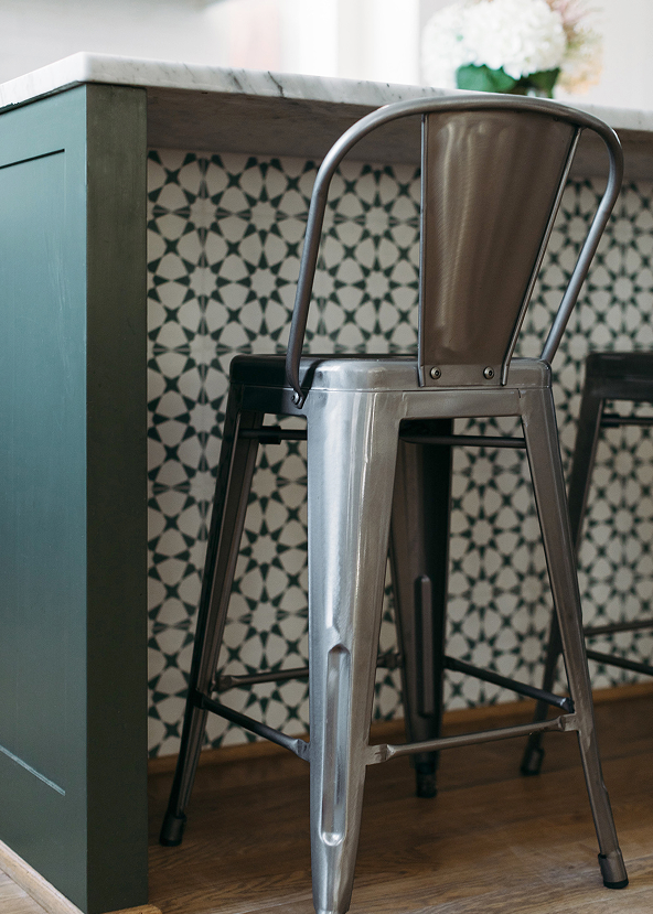 Metal bar stool in a kitchen setting with patterned backsplash and marble countertop.