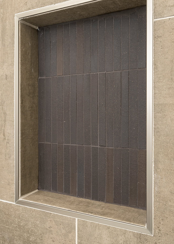 Tiled shower niche with dark tiles and a light-colored frame.