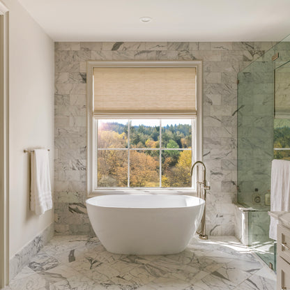 Modern bathroom with a freestanding bathtub, marble walls, and a window view of trees.