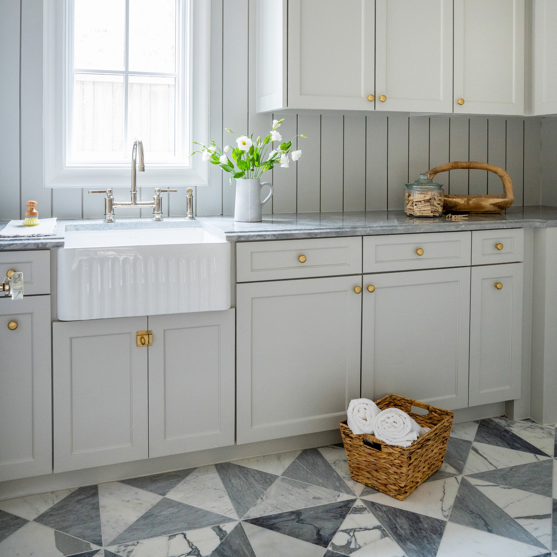Modern kitchen with gray cabinets, white sink, and marble flooring.
