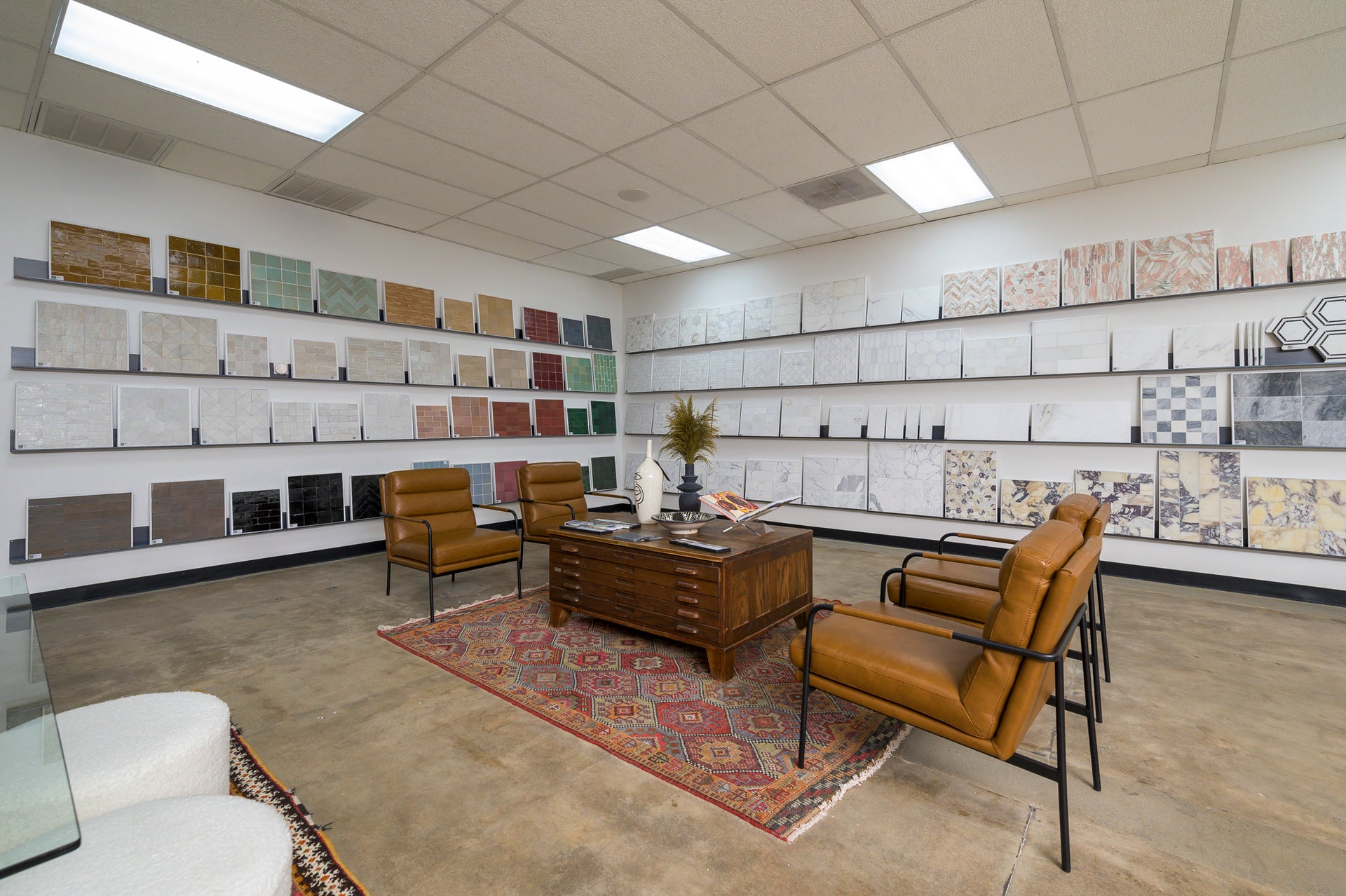 Interior showroom of Riad Tile displaying a wide variety of tile samples on wall racks with seating area and table in the center.