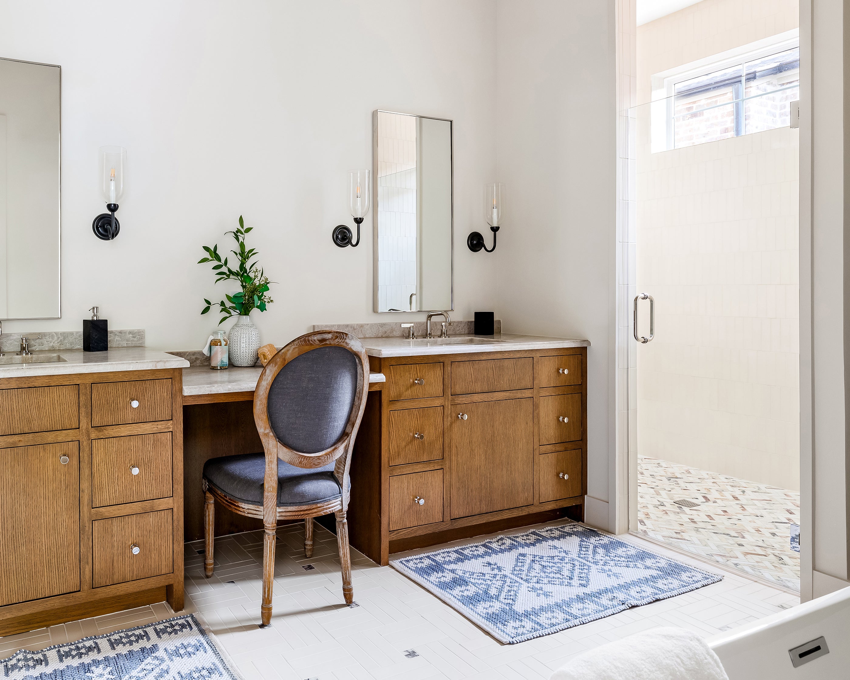 Bathroom with wooden vanity, chair, and walk-in shower. Off white ceramic tile flooring.