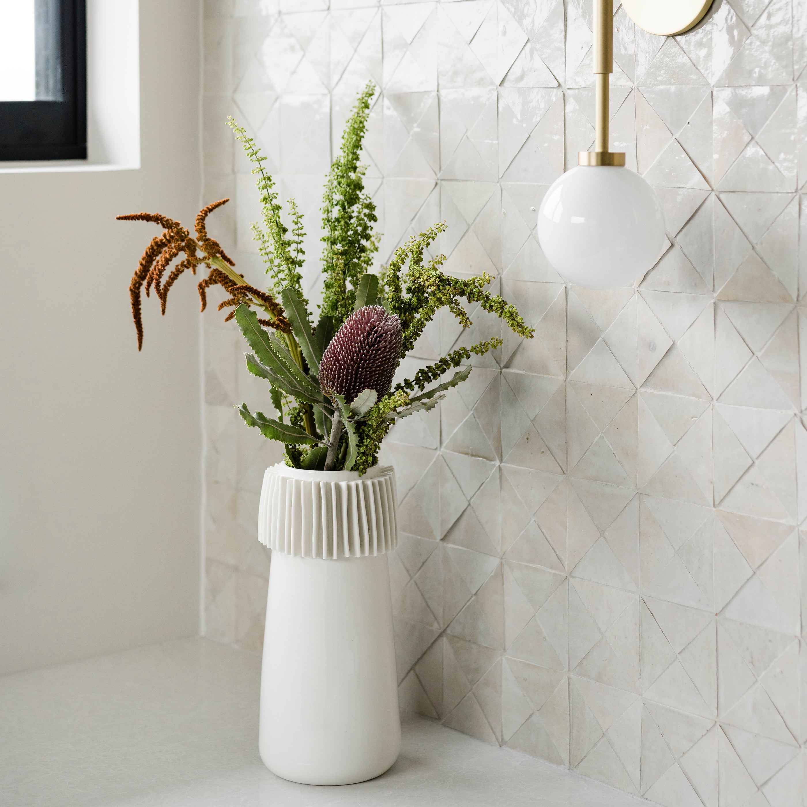 White vase with green plants against a geometric zellige tile wall