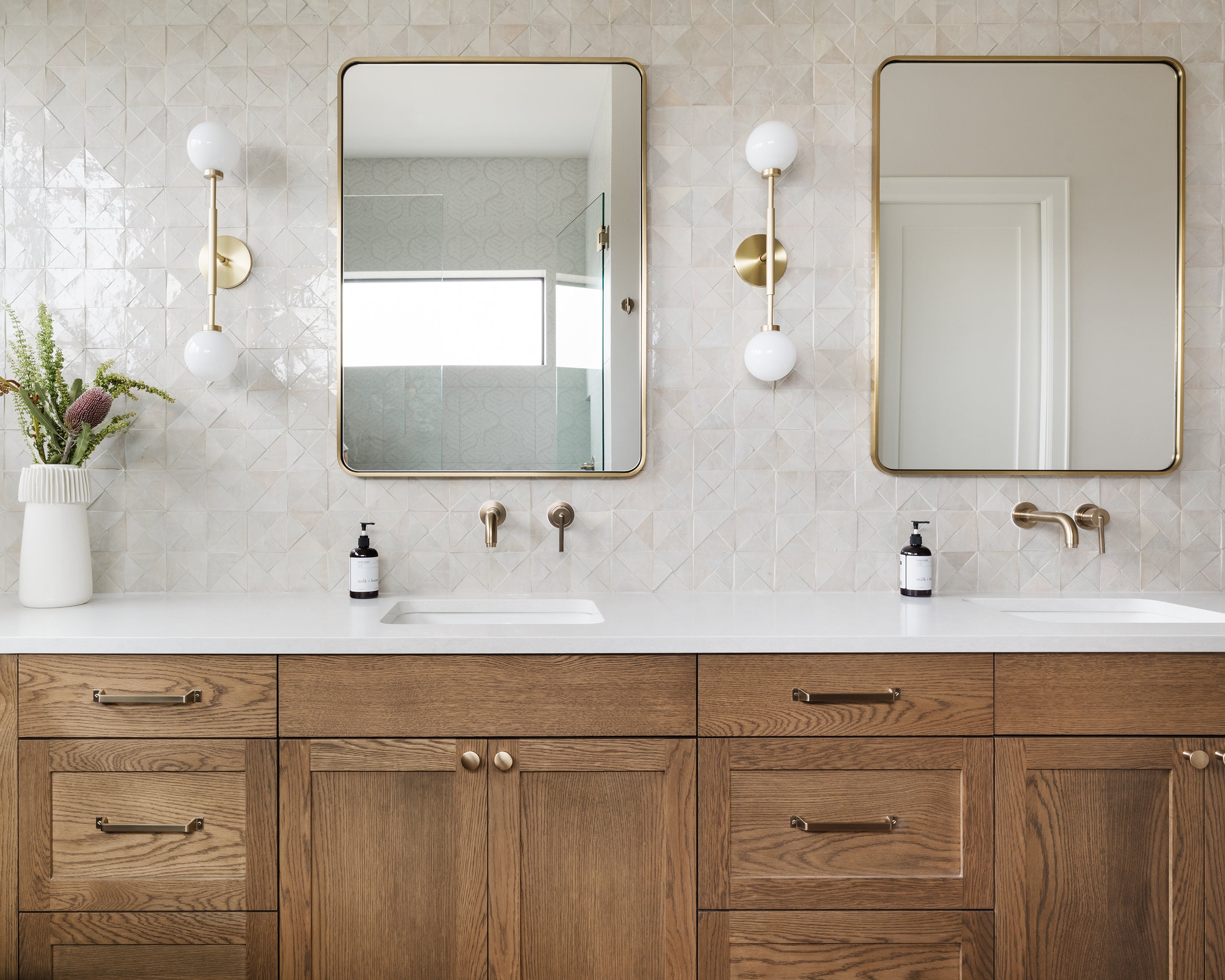 Bathroom with wooden vanity, white countertop, two mirrors, and zellige tile wall.