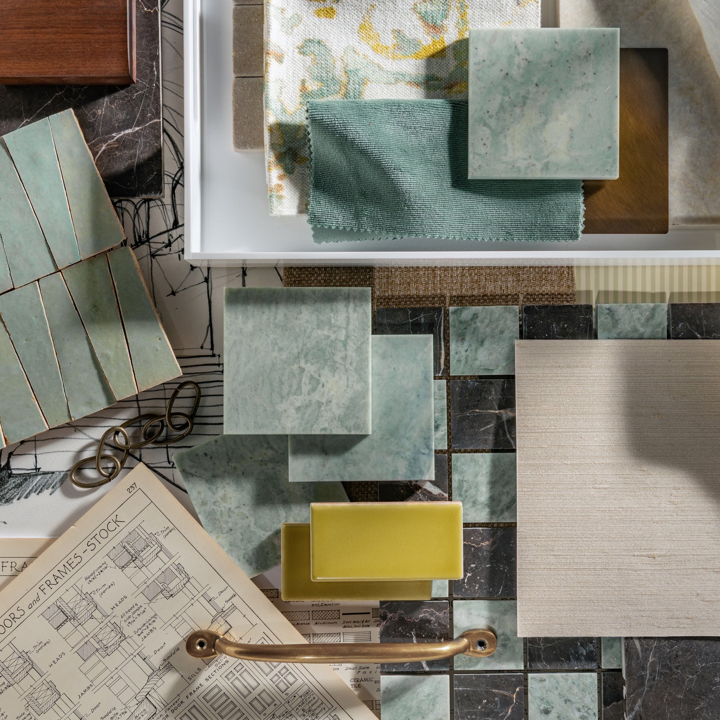 A styled flat-lay of home decor and marble and zellige materials, featuring square tiles and fabric and tile swatches in sage green, cream, and yellow, alongside a brass handle, architectural drawings, and wood textures.