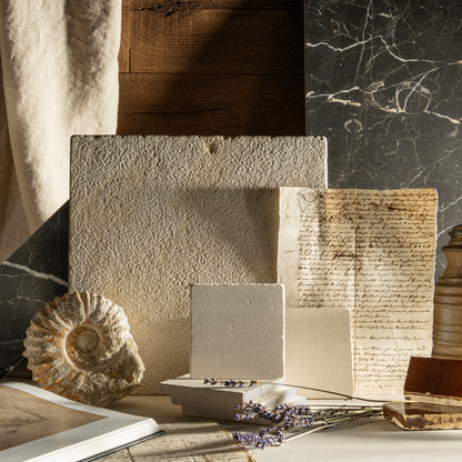 Collection of textured limestone and marble tiles and books on a marble surface with a natural light setting.