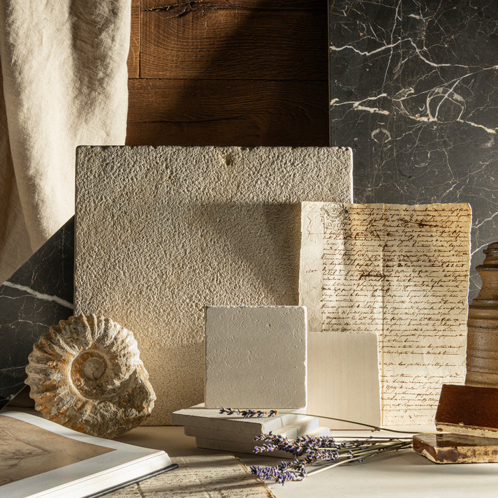 Collection of textured limestone and marble tiles and books on a marble surface with a natural light setting.