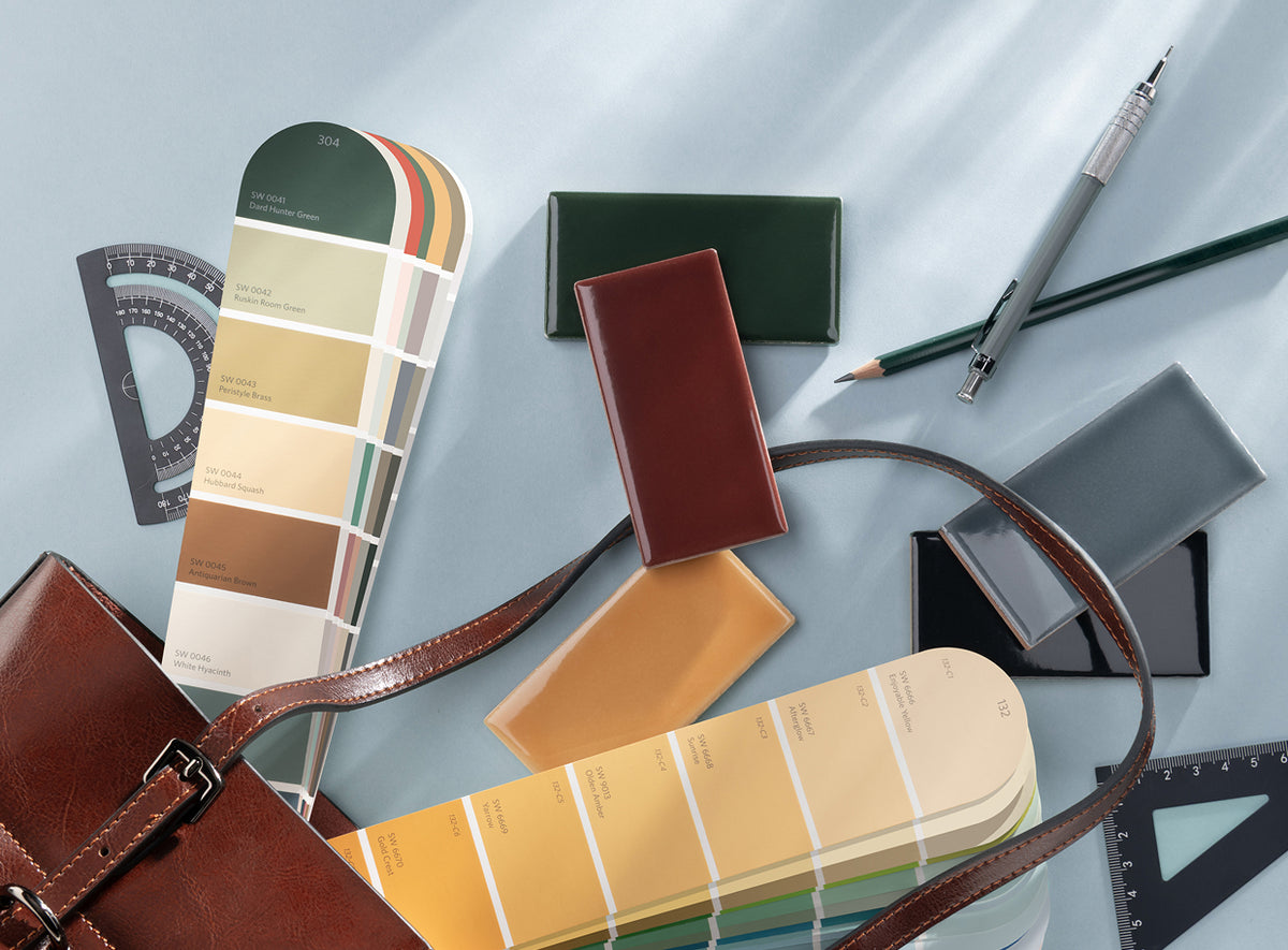 A styled flat-lay featuring two color swatch fans, a brown leather handbag strap, and various colored cardstock swatches on a light blue background, alongside a mechanical pencil, a pencil eraser, and geometric rulers.