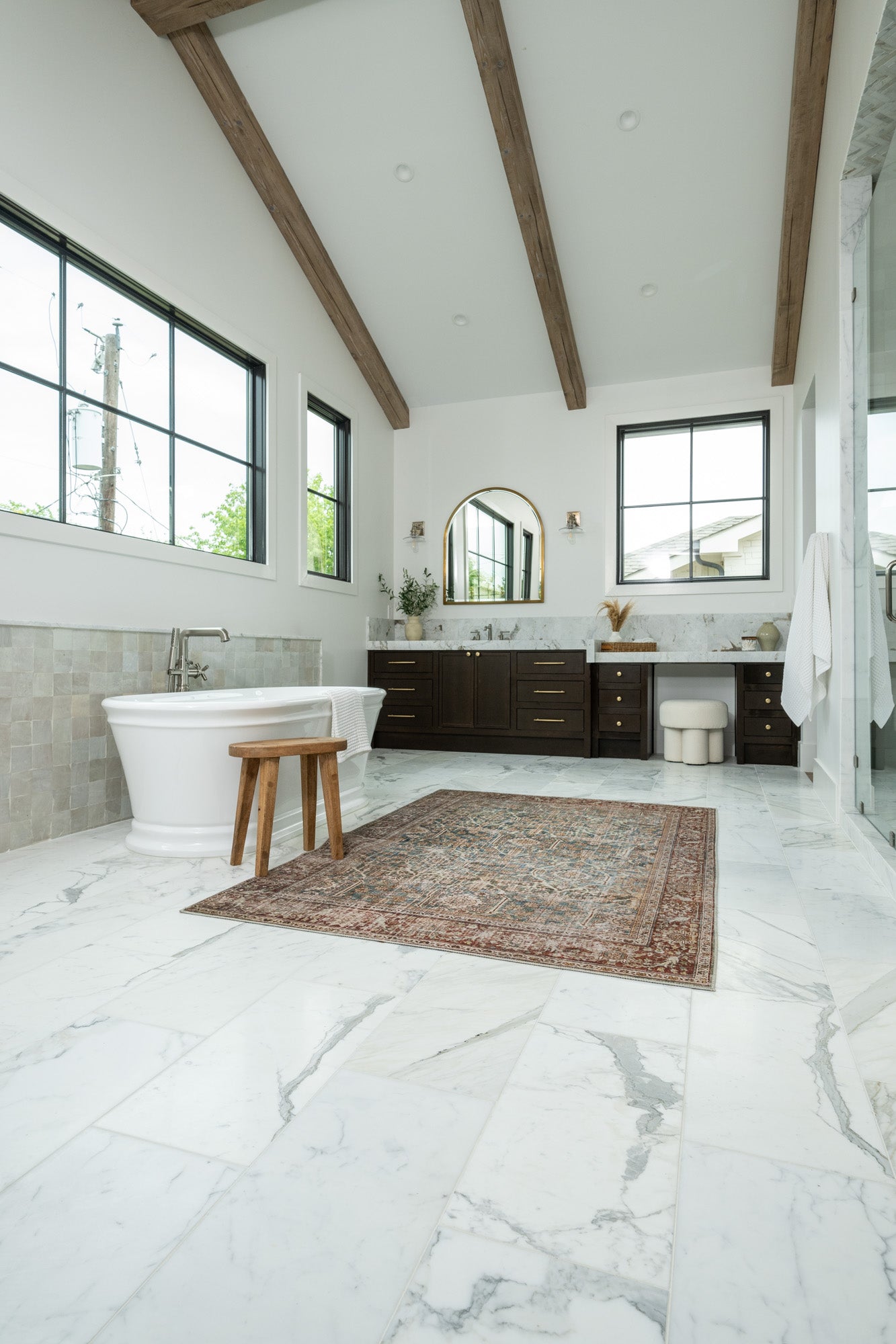 a spacious bathroom with large-format natural stone tiles on the floor, combined with wooden beams on the ceiling and a freestanding bathtub, emphasizing a blend of rustic and modern design elements