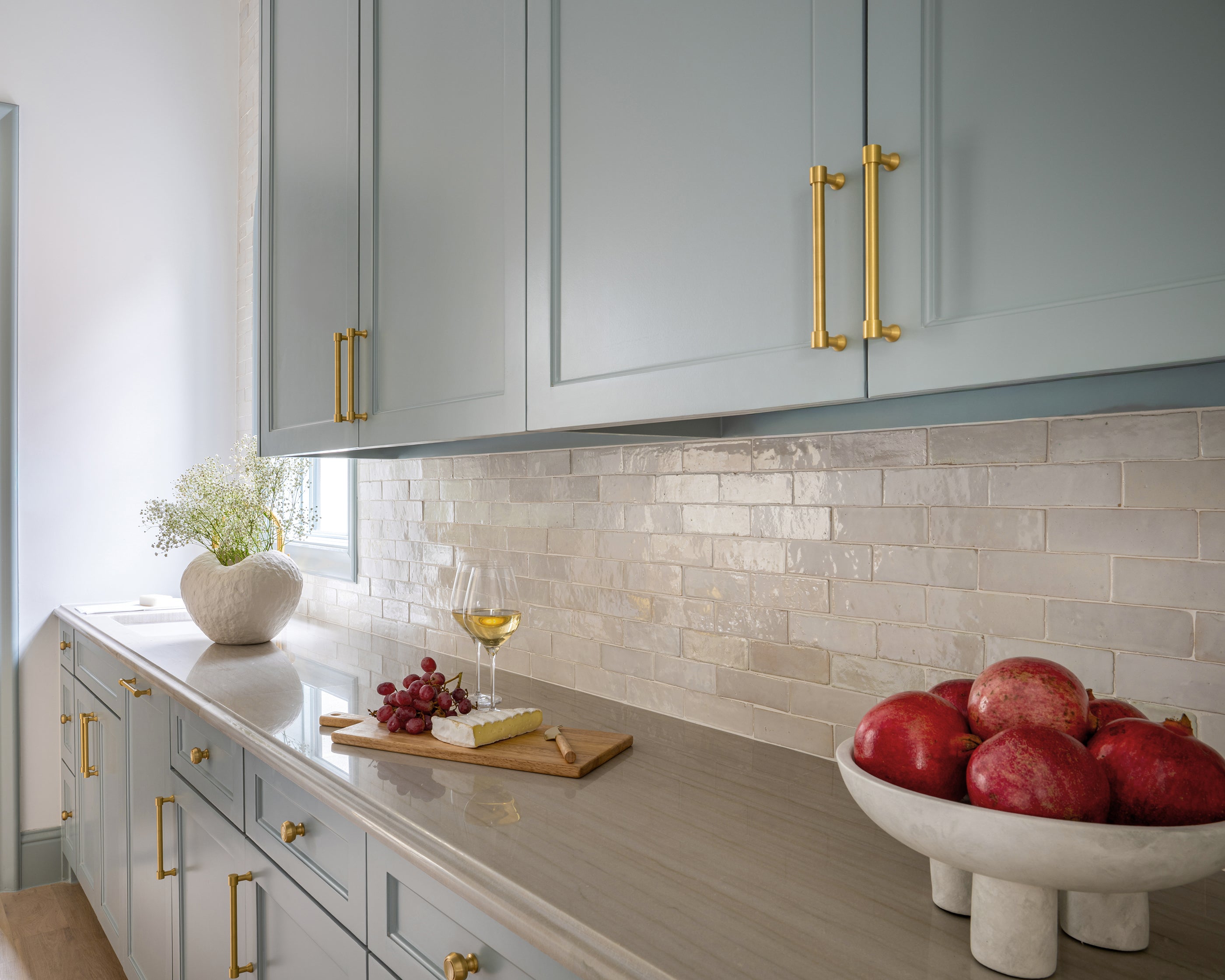 Modern kitchen with light gray cabinets, gold handles, and zellige backsplash tile.