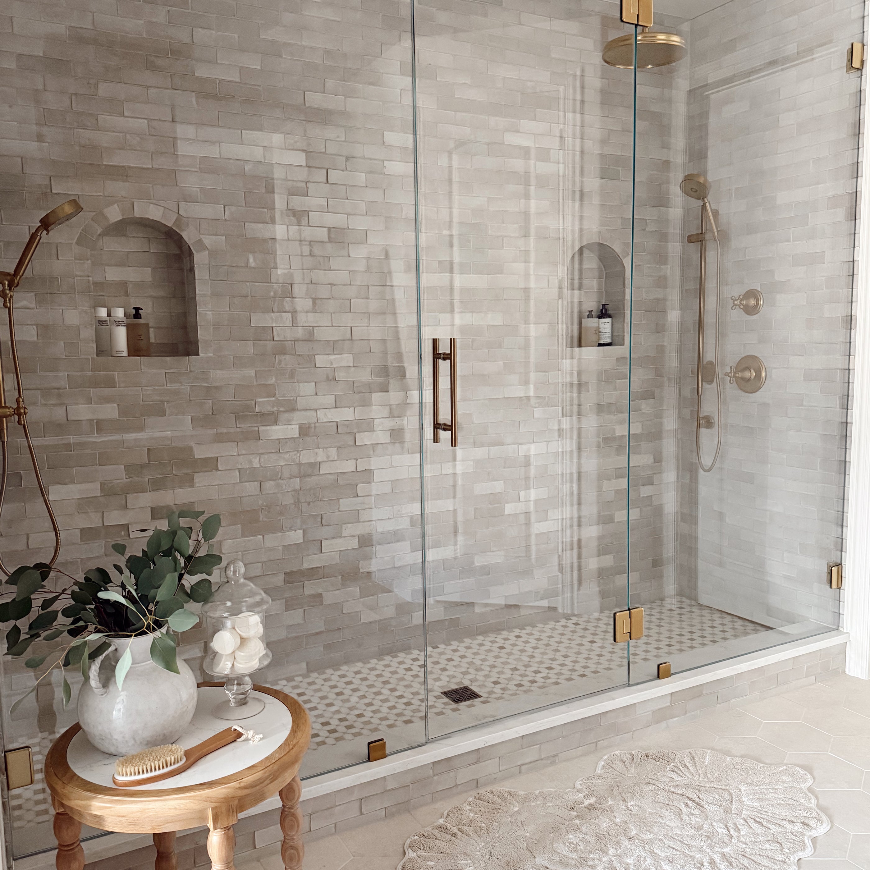 Modern bathroom with glass shower enclosure, zellige tiled walls, and a small table with decorative items.