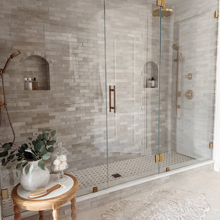 Modern bathroom with glass shower enclosure, zellige tiled walls, and a small table with decorative items.